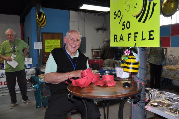 Volunteer smiles while holding raffle tickets at Danville Project Literacy’s JeopardBee event, seated beside a bright 50/50 raffle sign and bee-themed decorations.