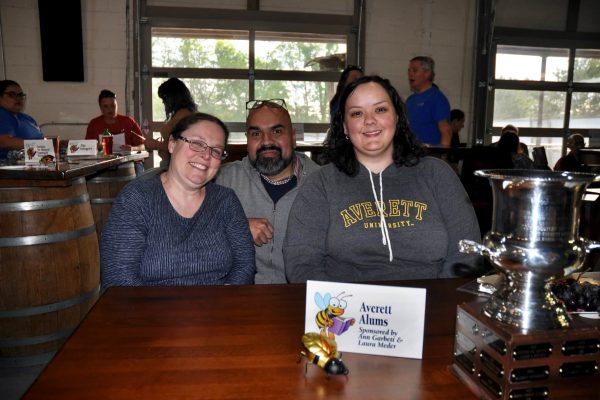 Averett Alums team members smile at their table beside a JeopardBee sponsor sign and trophy.