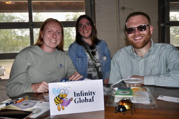 Infinity Global team members smile at their table with JeopardBee materials and bee-themed decorations.