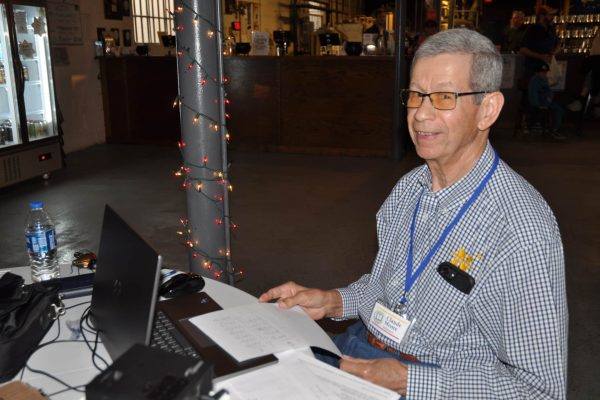 JeopardBee volunteer sits at a registration or scoring table with a laptop, papers, and event materials during Danville Project Literacy’s fundraiser.