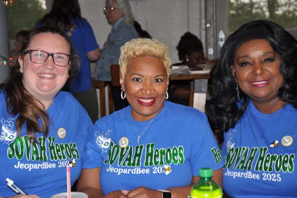Three participants wearing “SOVAH Heroes JeopardBee 2025” shirts smile together at a table during the Danville Project Literacy event.